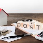 A person stands in front of a house, looking contemplative and holding a sign that reads, "I don't want to sell my house