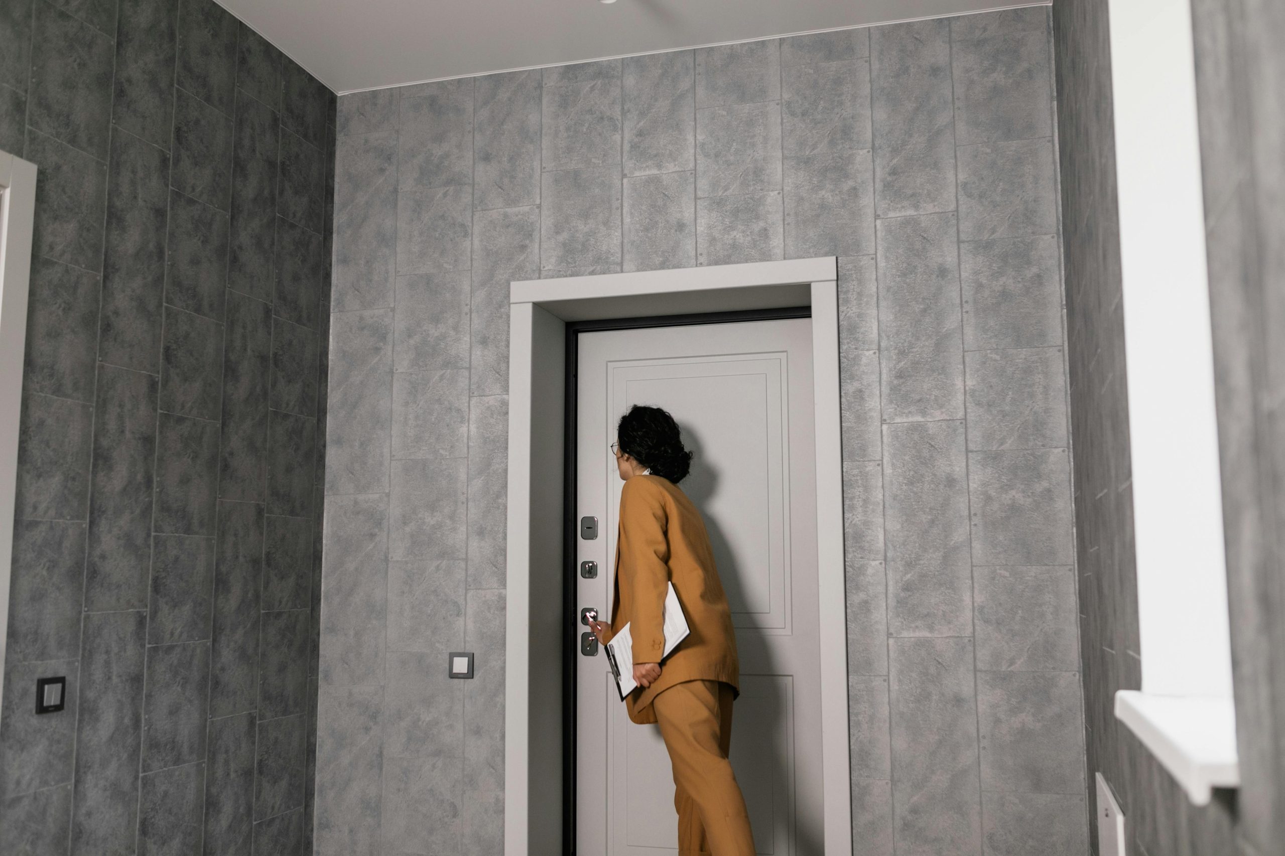 A woman stands in the doorway of a room, looking out with a neutral expression.